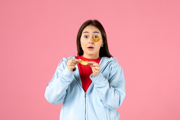 Vorderansicht einer jungen Frau, die eine Maske für ihr Gesicht an einer rosa Wand macht?