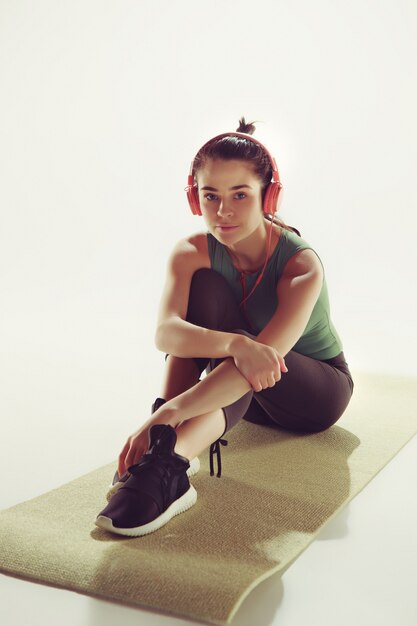 Vorderansicht einer jungen Frau, die mit Kopfhörern in der Gymnastikklasse sitzt.