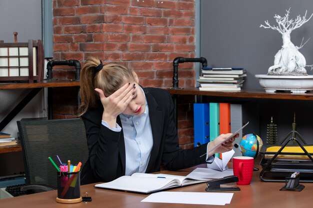 Vorderansicht einer jungen Frau in tiefen Gedanken, die an einem Tisch sitzt und ein Dokument im Büro hält