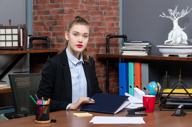 Vorderansicht einer jungen selbstbewussten Assistentin, die an ihrem Schreibtisch im Büro sitzt