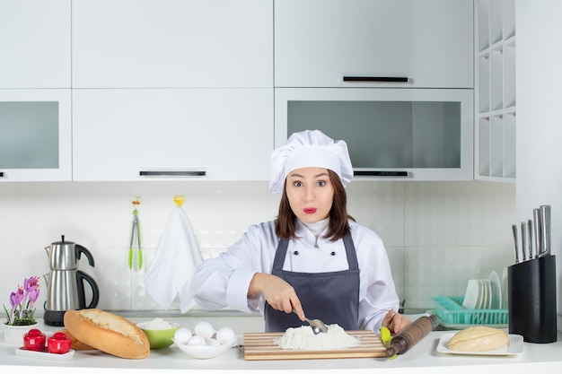 Vorderansicht einer jungen selbstbewussten Köchin in Uniform, die Essen in der weißen Küche zubereitet