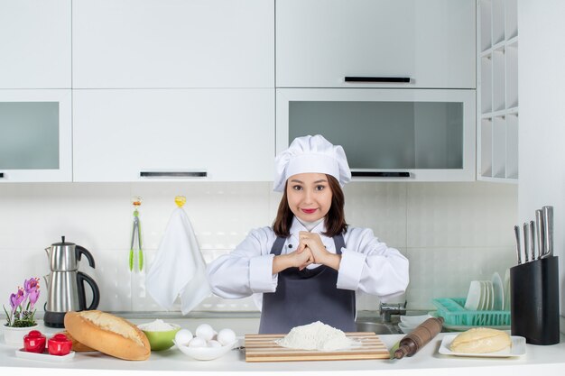 Vorderansicht einer jungen selbstbewussten Köchin in Uniform, die in der weißen Küche für die Kamera posiert