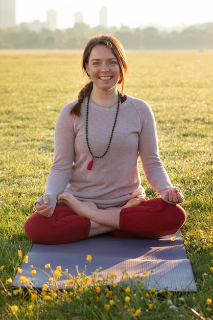 Kostenloses Foto vorderansicht einer smiley-frau, die im freien auf einer yogamatte meditiert