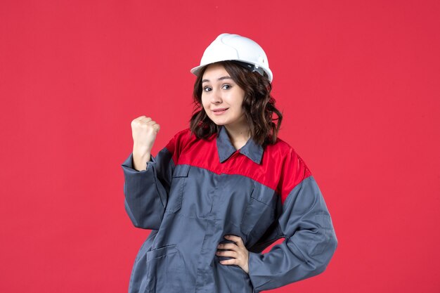 Vorderansicht einer stolzen Baumeisterin in Uniform mit Schutzhelm auf isoliertem rotem Hintergrund