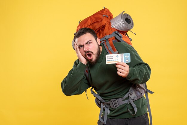 Vorderansicht eines emotional nervösen reisenden Kerls mit Rucksack und Ticket auf gelbem Hintergrund