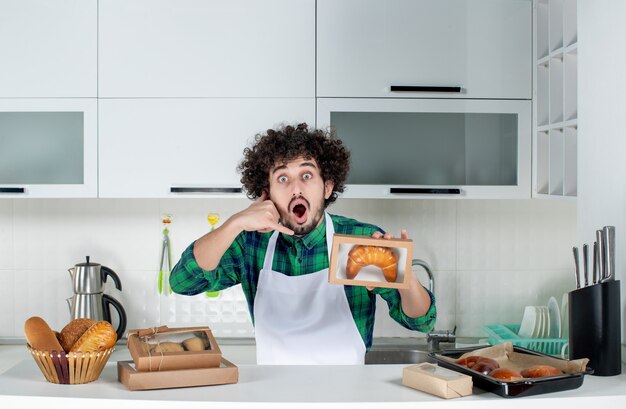 Vorderansicht eines emotional überraschten Mannes, der frisch gebackenes Gebäck in einer kleinen Schachtel zeigt und mich in der weißen Küche anruft