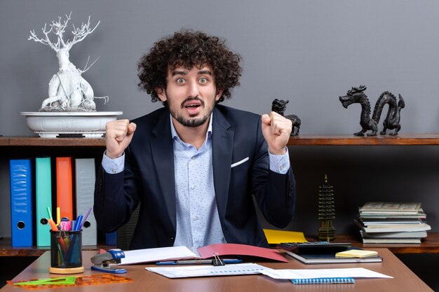 Vorderansicht eines glücklichen Büroangestellten, der eine gewinnende Geste zeigt, die am Schreibtisch im Büro sitzt