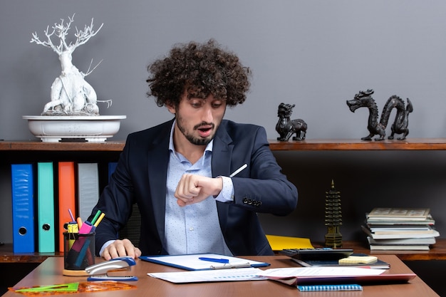 Vorderansicht eines jungen Geschäftsmannes, der am Schreibtisch sitzt und die Zeit überprüft