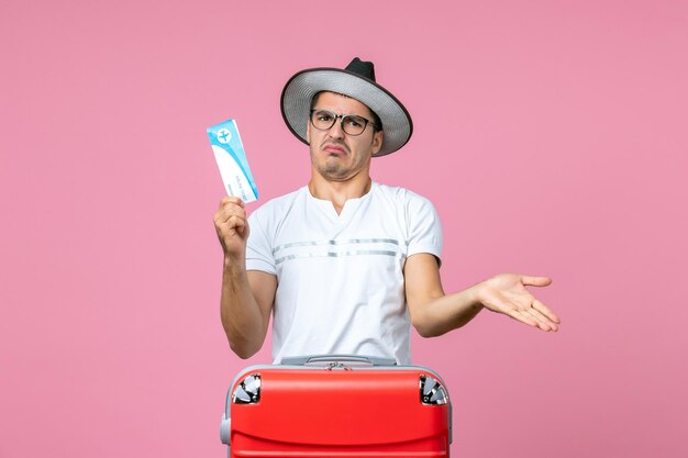 Vorderansicht eines jungen Mannes, der ein Flugticket für den Urlaub an der rosa Wand hält