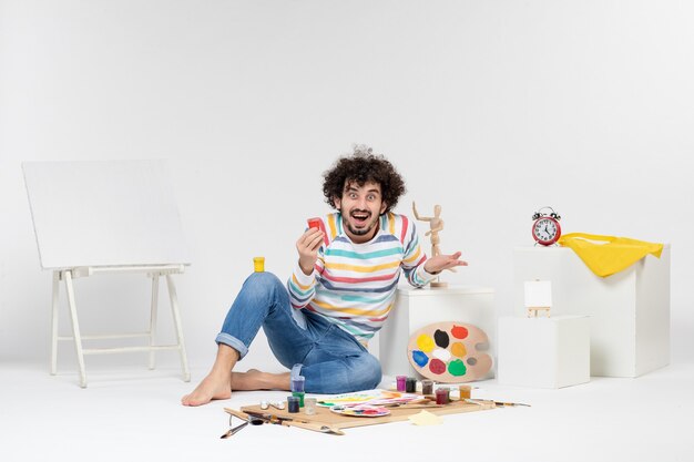 Vorderansicht eines jungen Mannes, der Farben zum Zeichnen in eine kleine Dose an einer weißen Wand hält