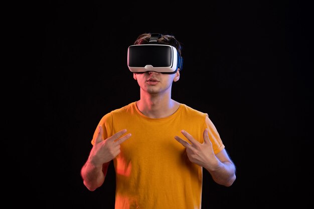 Vorderansicht eines jungen Mannes mit VR-Headset an der dunklen Wand