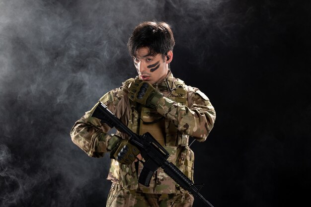 Vorderansicht eines männlichen Soldaten in Tarnung, der auf eine schwarze Wand zielt
