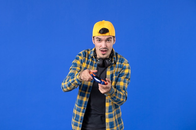 Kostenloses Foto vorderansicht eines männlichen spielers mit orangefarbenem gamepad an blauer wand