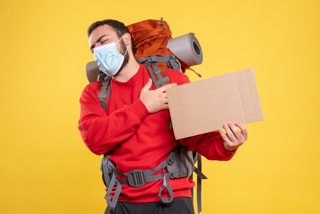 Vorderansicht eines Reisenden, der eine medizinische Maske mit einem Rucksack trägt, der ein Blatt zeigt, ohne auf gelbem Hintergrund zu schreiben