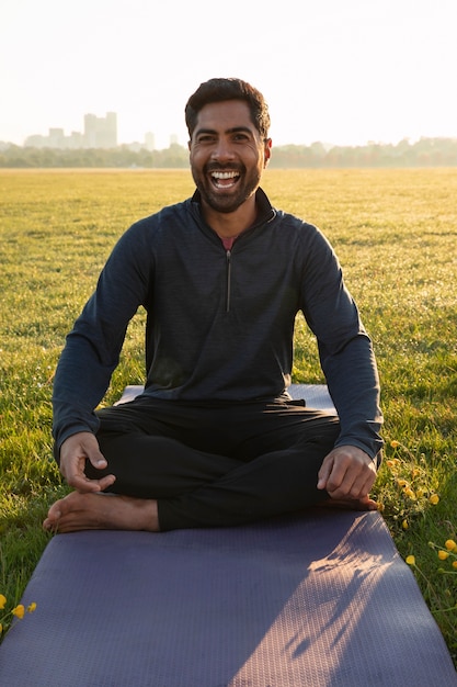 Kostenloses Foto vorderansicht eines smiley-mannes, der draußen auf einer yogamatte meditiert