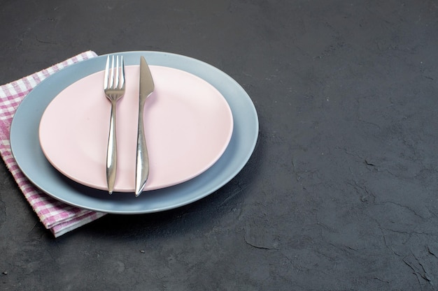 Vorderansicht eleganter rosa Teller mit blauem Tellermesser und Gabel auf dunkel