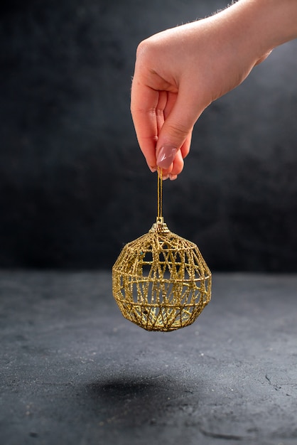 Vorderansicht Fadenschnur goldener Weihnachtsbaumball in weiblicher Hand auf dunklem, isoliertem Hintergrund