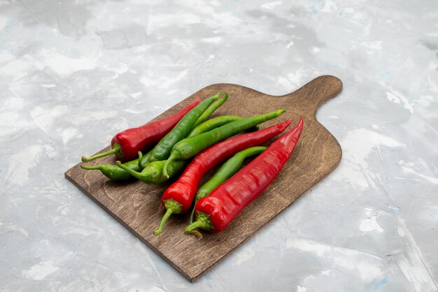 Vorderansicht färbte würzige Paprika grün und rot auf dem hellen Schreibtischgewürz der heißen Gemüsezutat