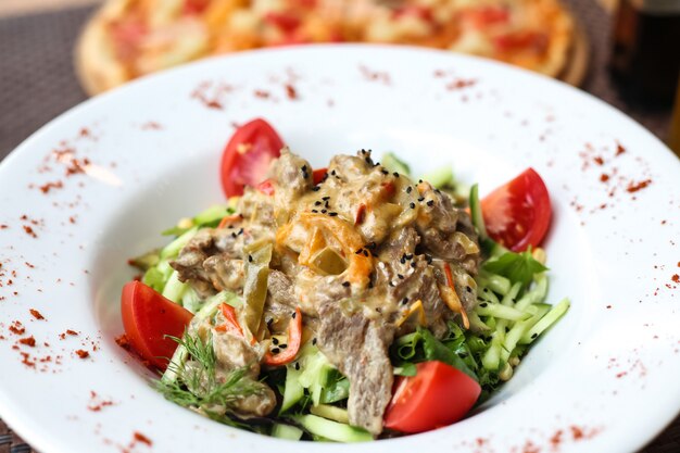 Vorderansicht Fleischsalat mit geschnittenen Gurken und Tomaten auf einem Teller mit Gewürzen