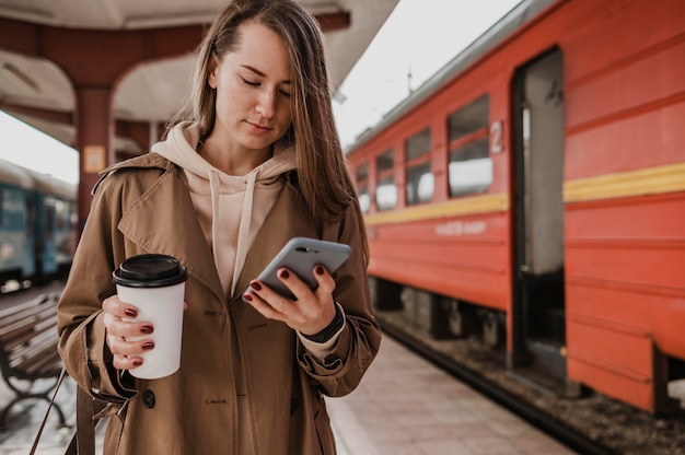 Kostenloses Foto vorderansicht frau, die eine tasse kaffee am bahnhof hält