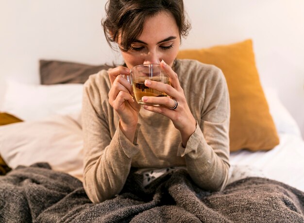 Vorderansicht Frau, die ihren Tee im Bett trinkt