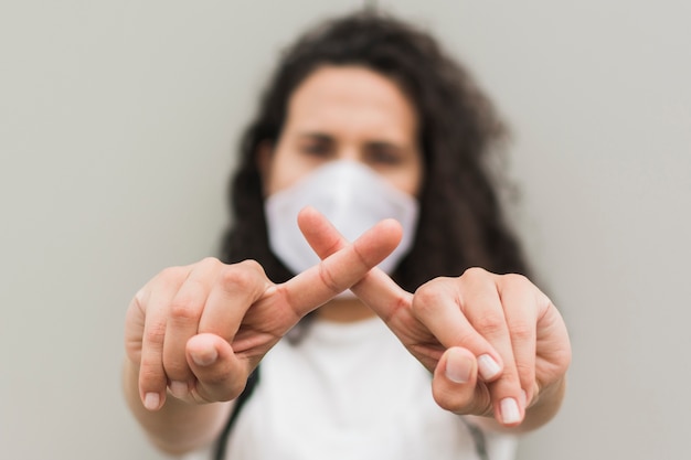 Kostenloses Foto vorderansicht frau, die medizinische maske trägt und ein x mit ihren fingern bildet