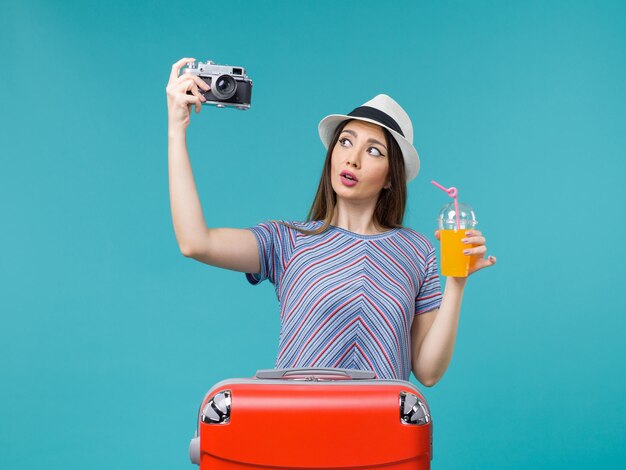 Vorderansicht Frau im Urlaub hält Saft und Kamera auf dem blauen Hintergrund Seereise Sommerreise Reise Urlaub