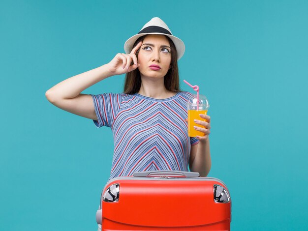 Vorderansicht Frau im Urlaub mit ihrer roten Tasche, die ihren Saft auf dem blauen Hintergrundreise-Sommerseereise-Reiseurlaub hält