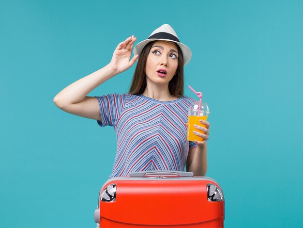 Vorderansicht Frau im Urlaub mit ihrer roten Tasche, die ihren Saft auf dem blauen Hintergrundreise-Sommerseereise-Reiseurlaub hält