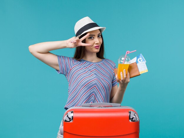 Vorderansicht Frau im Urlaub mit ihrer roten Tasche, die Tickets und Saft auf der blauen Hintergrundreise Reisereise weibliche Reise hält