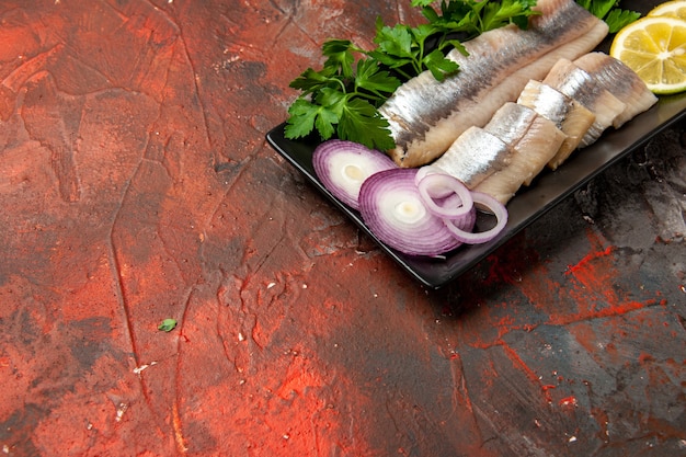 Kostenloses Foto vorderansicht frisch geschnittener fisch mit gemüse und zwiebeln in der schwarzen pfanne auf dunklem snack-mahlzeit-meeresfrüchte-foto