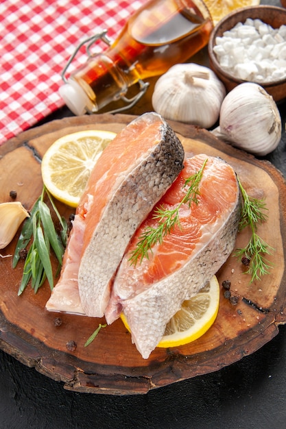 Vorderansicht frische Fischscheiben mit Zitronenscheiben Knoblauch und Gewürzen auf dunklem Fischgericht Farbe Lebensmittel Fleisch Foto roh