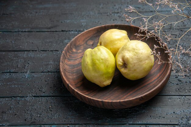 Vorderansicht frische reife Quitten saure Früchte innerhalb des Tellers auf dunkelblauem rustikalem Schreibtischpflanzenobst reifer frischer Baum