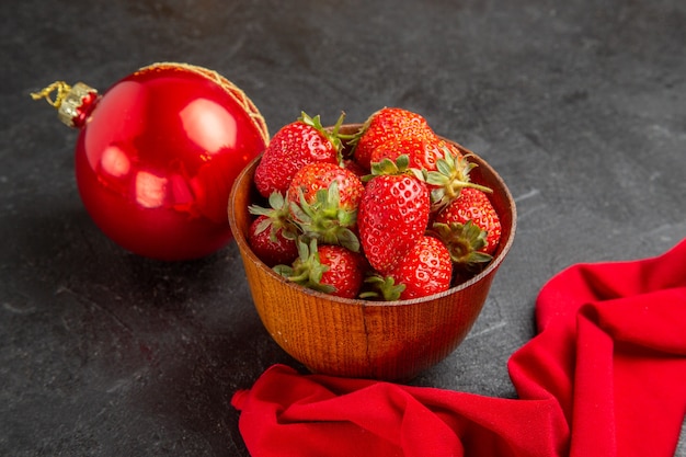 Vorderansicht frische rote Erdbeeren innerhalb des Tellers mit Spielzeug auf dunklem Hintergrund viele Fruchtfotos milde Farbe