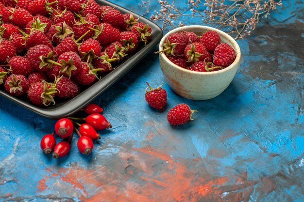 Vorderansicht frische rote Himbeeren im schwarzen Tablett auf blauem Hintergrund Pflanzenbaumfarbe Beere wilde reife Früchte