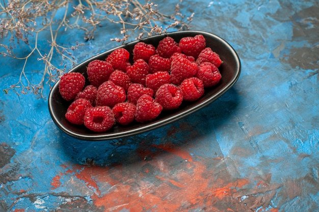 Vorderansicht frische rote Himbeeren in schwarzer Platte auf blauem Hintergrund Fruchtfoto Pflanze Baumfarbe wilde reife Beere