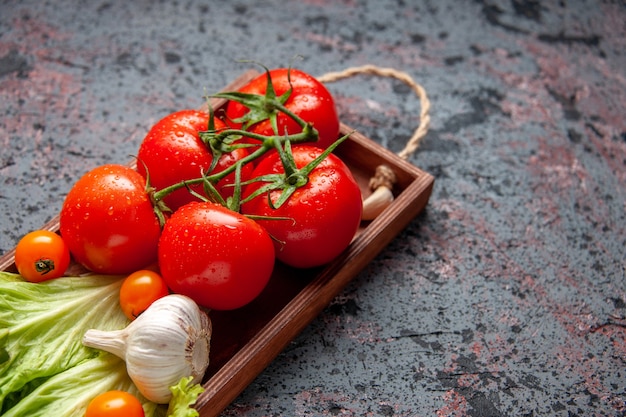 Vorderansicht frische rote Tomaten mit Knoblauch und grünem Salat innerhalb Holzbrett auf blauem Hintergrund