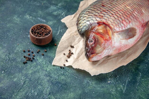 Vorderansicht frischer roher Fisch mit Pfeffer auf dunkelblauer Oberfläche Fleischwasser Ozeanfarbe horizontales Essen Meeresfrüchte Mahlzeit