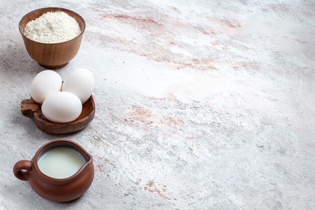 Vorderansicht ganze rohe Eier mit Mehl und Milch auf hellweißem Hintergrund Ei rohes Frühstück Mahlzeit Essen