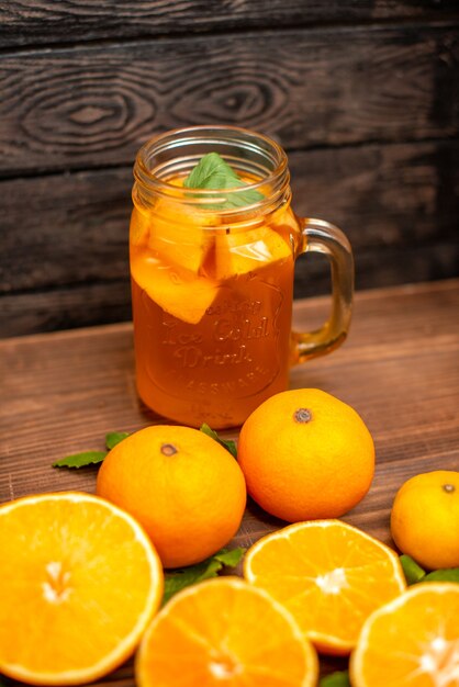 Vorderansicht ganzer und geschnittener frischer Orangen mit Blättern und natürlichem Saft in einem Glas auf braunem Hintergrund