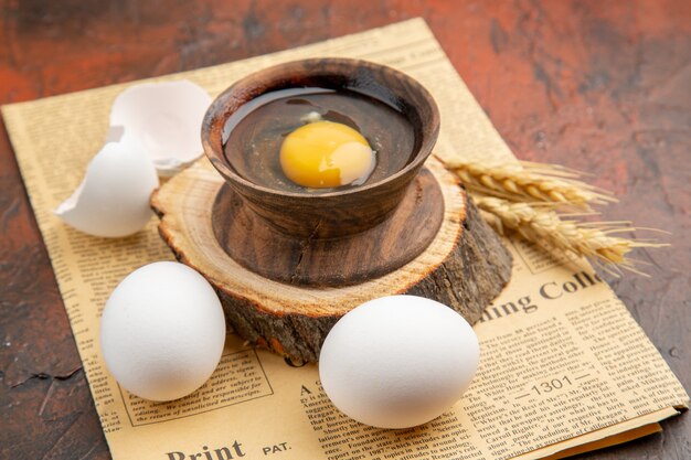 Vorderansicht gebrochenes rohes Ei innerhalb des Tellers mit anderen Eiern auf der dunklen Oberfläche