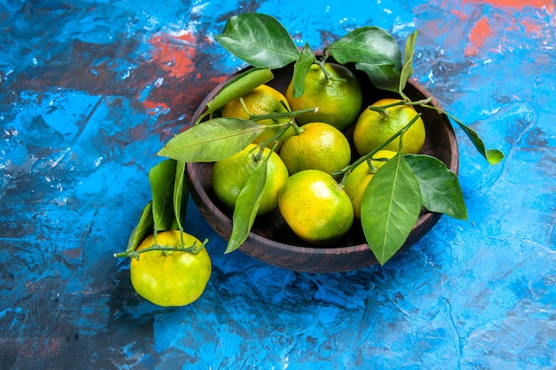 Vorderansicht gelbe Mandarinen mit Blättern in Holzschale eine Mandarine auf blauem Hintergrund