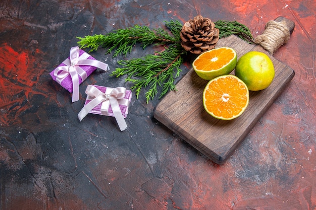 Vorderansicht geschnittene Orangen auf Schneidebrett Kiefernzweig mit Kegel-Weihnachtsgeschenken auf dunkelrotem Hintergrund Freiraum