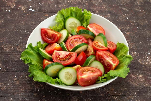 Vorderansicht geschnittene Tomaten mit Gurken in weißer Platte mit grünem Salat auf braunem, frischem Lald-Sald des Lebensmittelgemüses