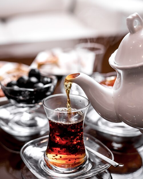 Vorderansicht gießt Tee in ein Glas Armudu aus einem Teekessel