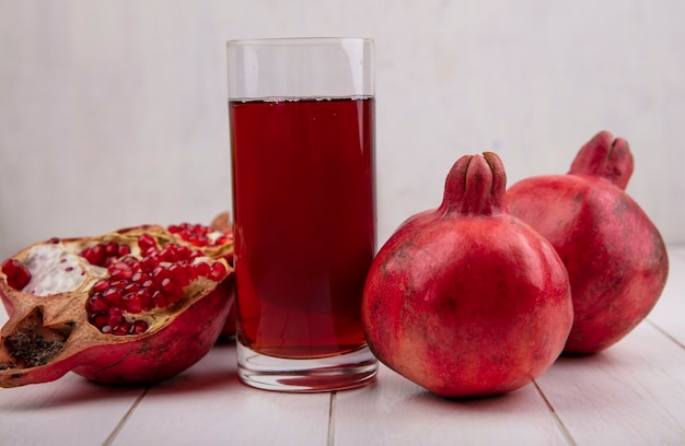 Kostenloses Foto vorderansicht glas granatapfelsaft mit granatäpfeln auf weißer wand