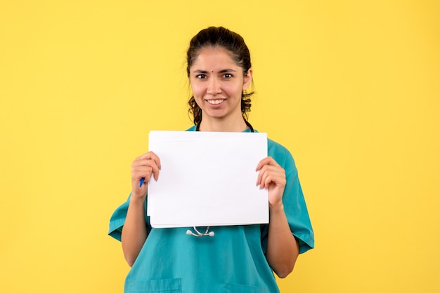 Vorderansicht glücklich hübsche Ärztin, die Papiere mit beiden Händen auf gelbem Hintergrund hält