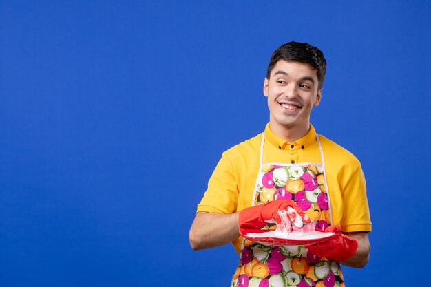 Vorderansicht glückliche männliche Haushälterin, die Platte auf blauem Raum wäscht