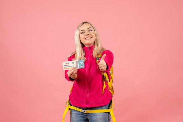 Vorderansicht glückliche reisende Frau in der Freizeitkleidung, die Rucksack hält Ticket hält Daumen hoch Zeichen