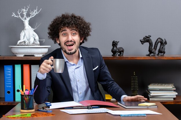 Vorderansicht glücklicher Geschäftsmann in formeller Kleidung, der am Schreibtisch im Büro sitzt